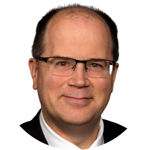 Studio headshot of a smiling man wearing glasses and a dark suit on a white background
