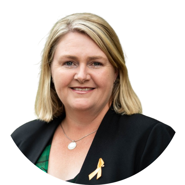 Portrait of a smiling woman in a black blazer with a green top and yellow ribbon pin