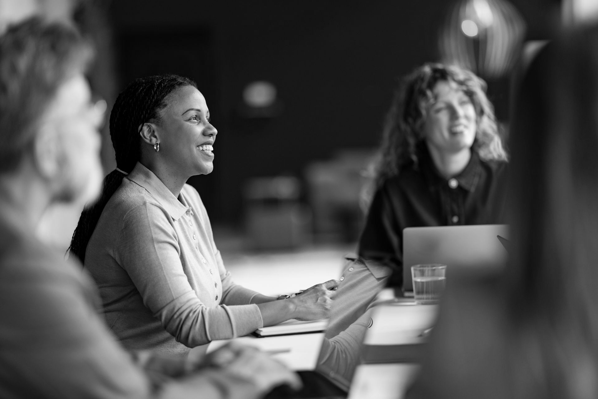 Three people in a meeting, talking around a table with a laptop in a black-and-white photo