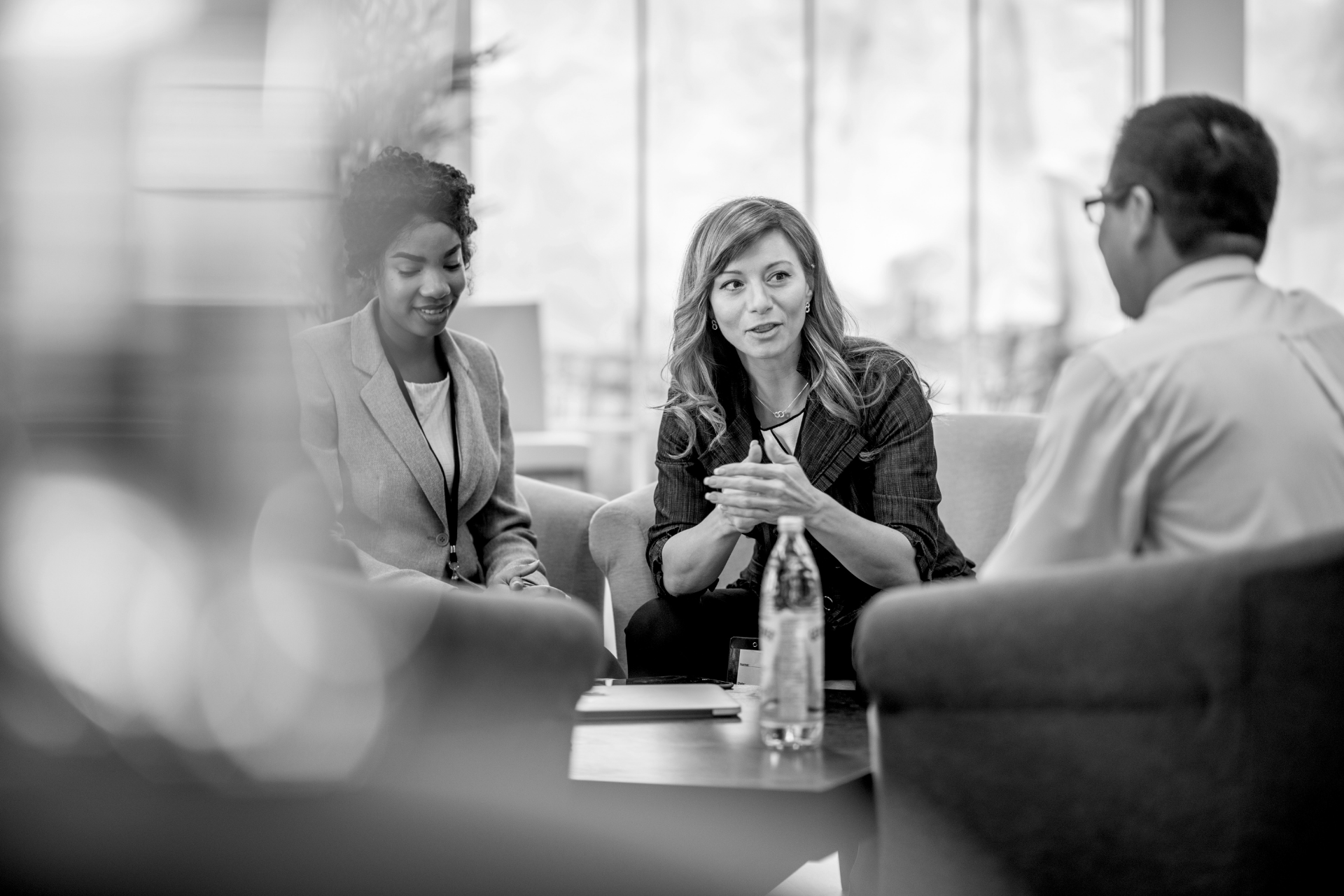 Three people in a meeting, seated around a table and talking in a bright office.