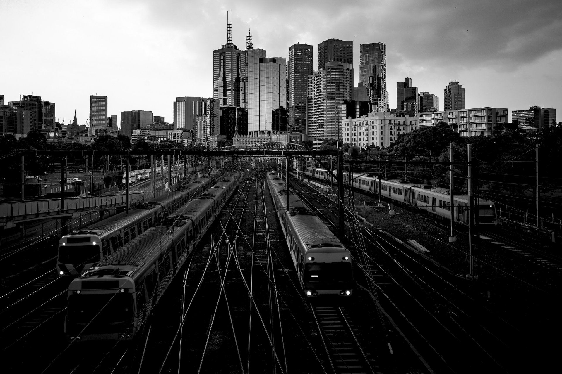 Black-and-white city skyline beyond railway tracks with multiple trains approaching the foreground