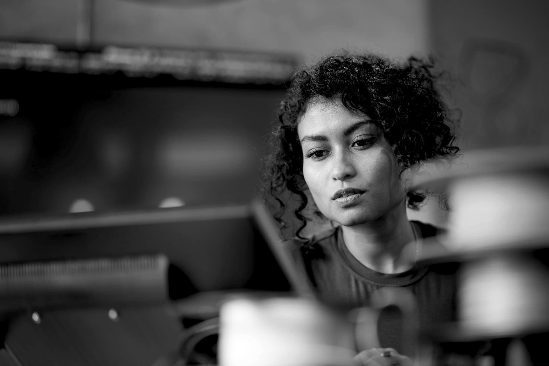 Person working at a laptop in a blurred office, looking thoughtfully at the screen.