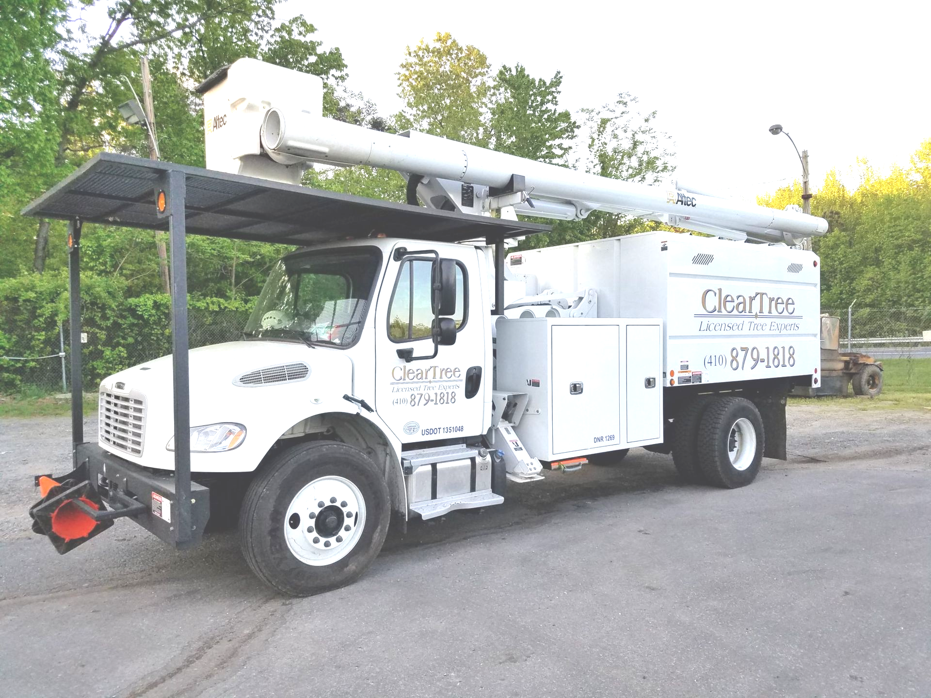 ClearTree White utility bucket truck parked on a road with an elevated boom arm and equipment boxes.
