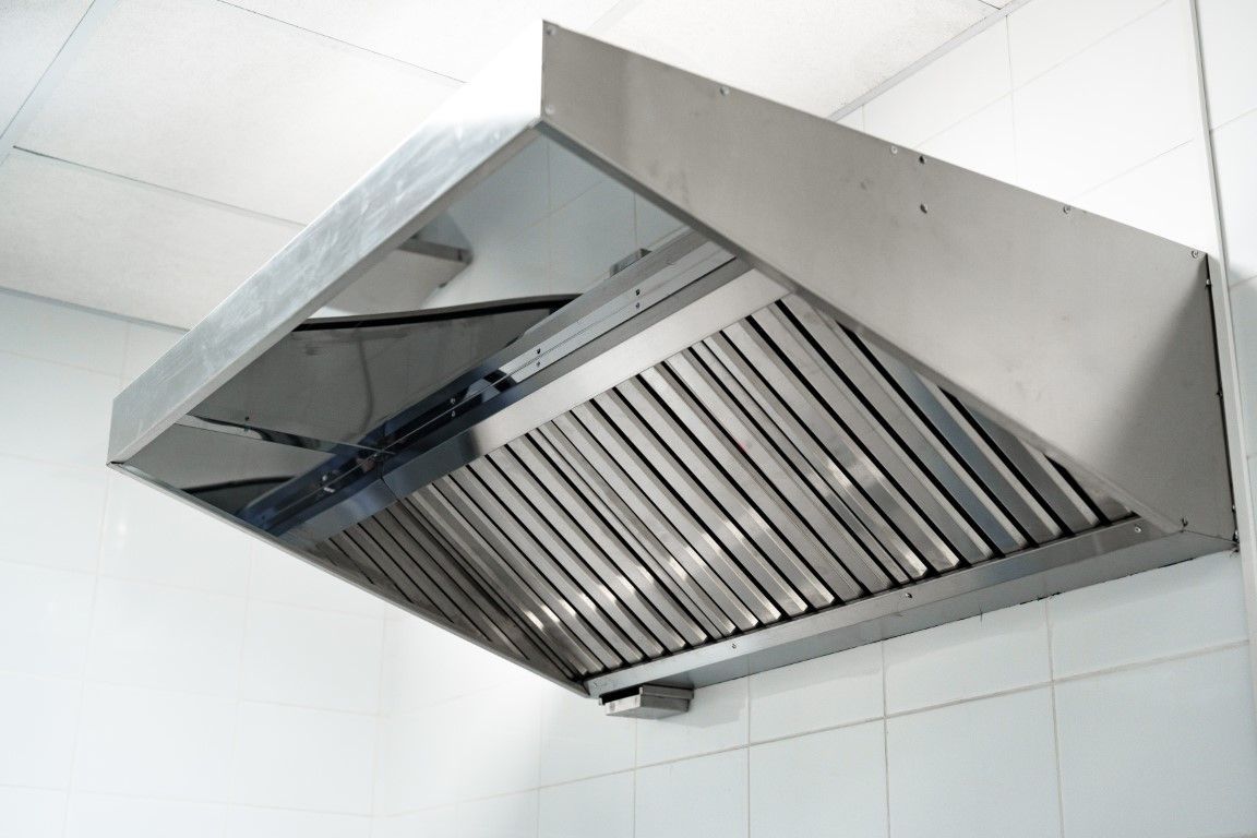 Stainless steel kitchen range hood mounted on a tiled wall, viewed from below.