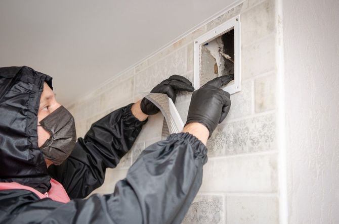 Technician cutting into a wall opening with a tool while wearing gloves and a hooded jacket