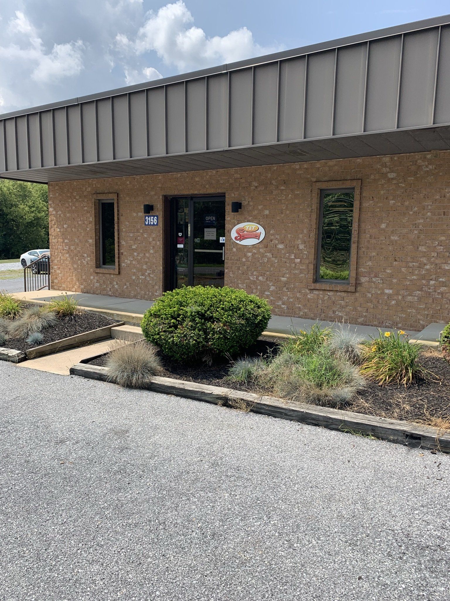 A brick building with a metal roof and a gravel driveway in front of it.