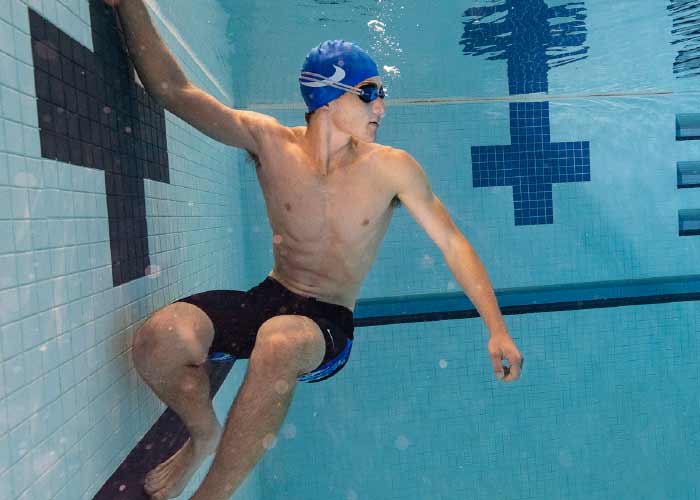 A shirtless man is swimming underwater in a pool