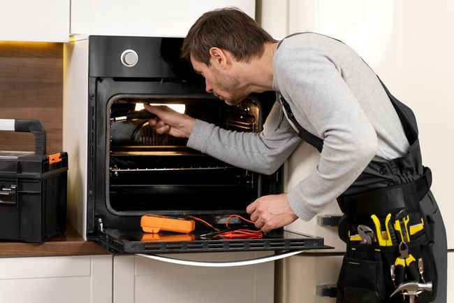 Technician inspecting a built-in oven with tools in a kitchen
