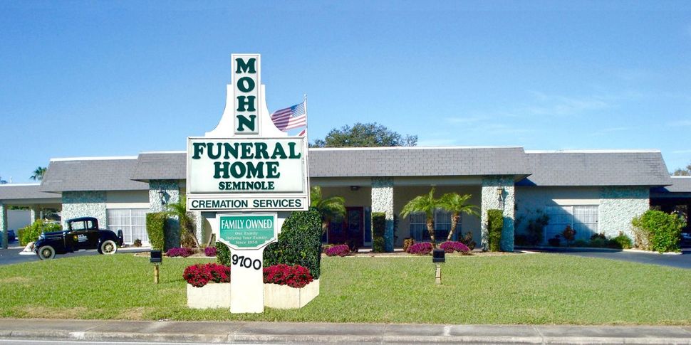Monh Funeral Home sign in front of a low building and lawn on a sunny day
