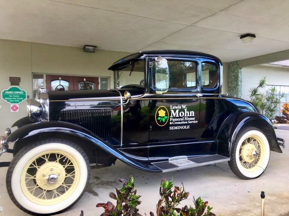 Vintage black coupe with whitewall tires parked under a covered entrance, branded “Mohn.”