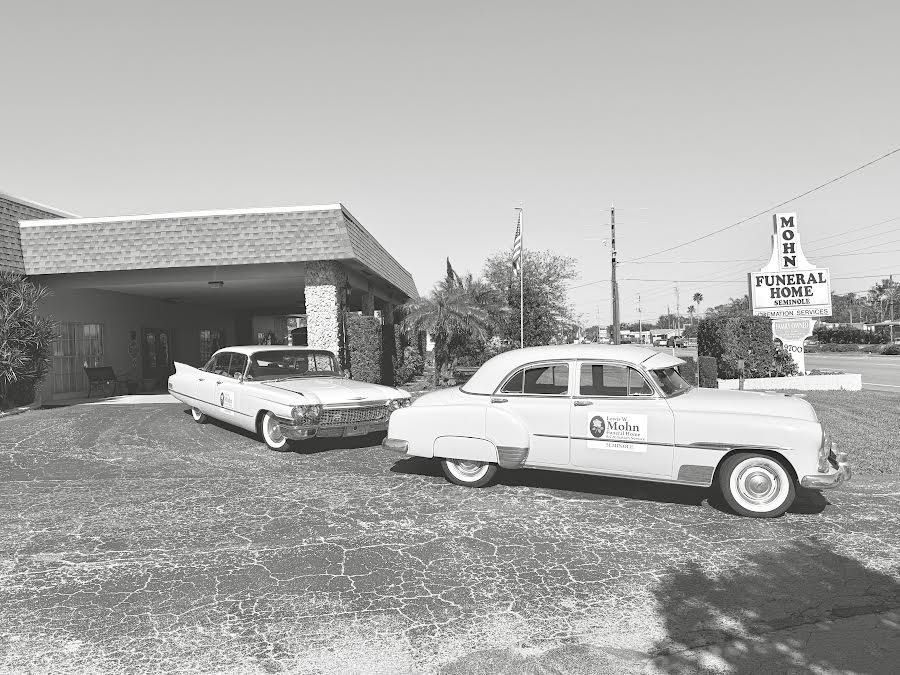 Two vintage cars parked outside a building with a sign, in a black-and-white scene