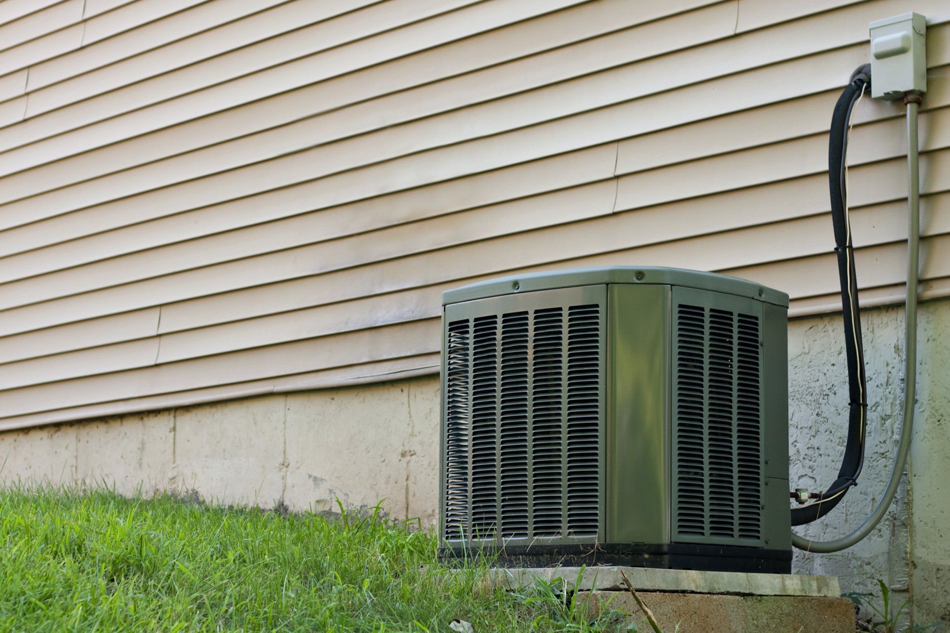 Air conditioner unit next to a beige house with green grass.