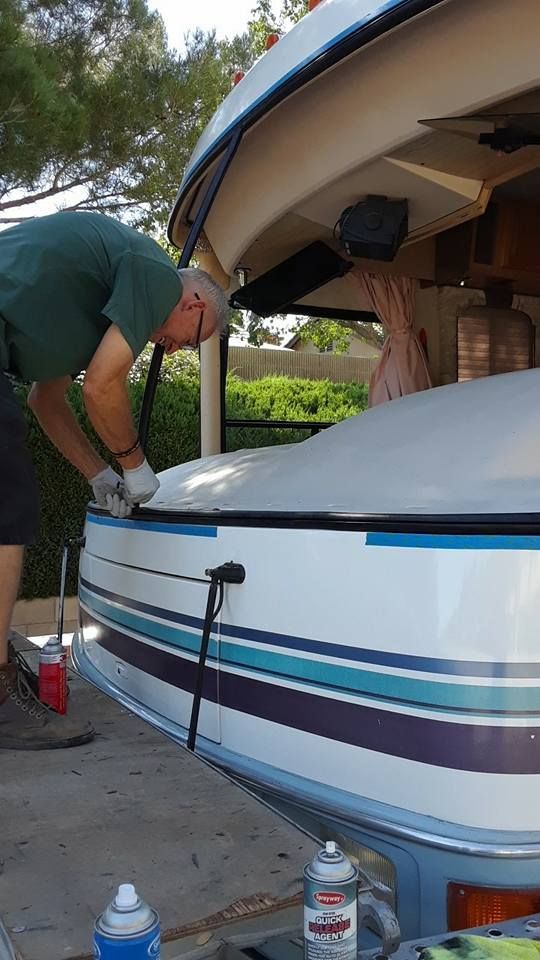 Person cleaning a white boat with blue stripes at a dock or driveway.
