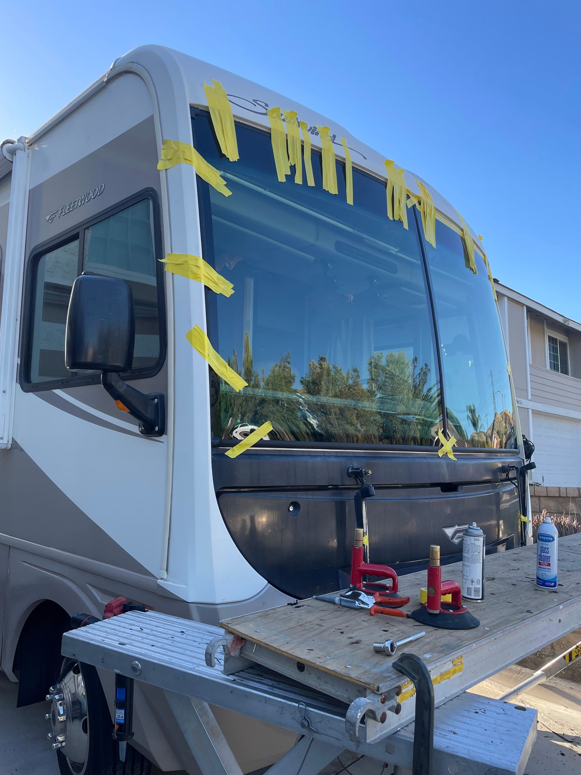 White RV motorhome with blue-tinted windshield parked outdoors, with painter’s tape masking the front windows.