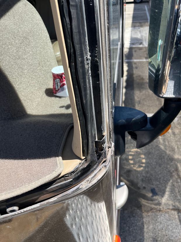 Close-up of a vehicle door frame and mirror with a soda can visible on the ground outside.