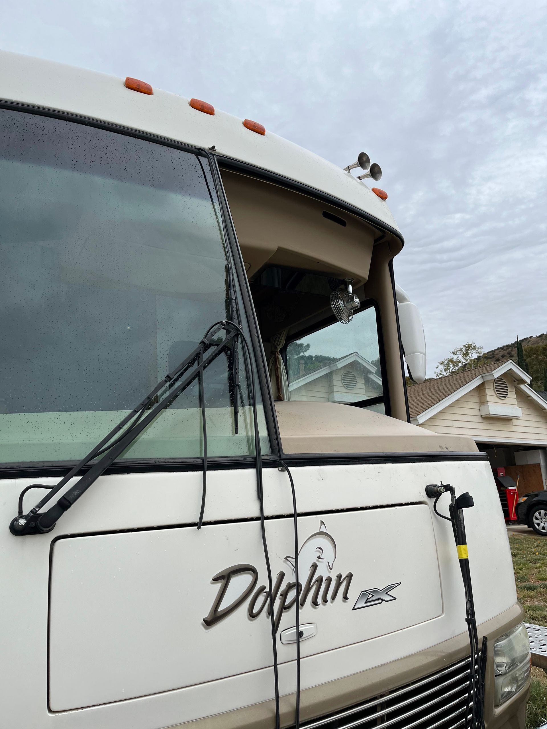 White Dolphin RV cab with windshield wipers and side logo, parked near houses under cloudy sky