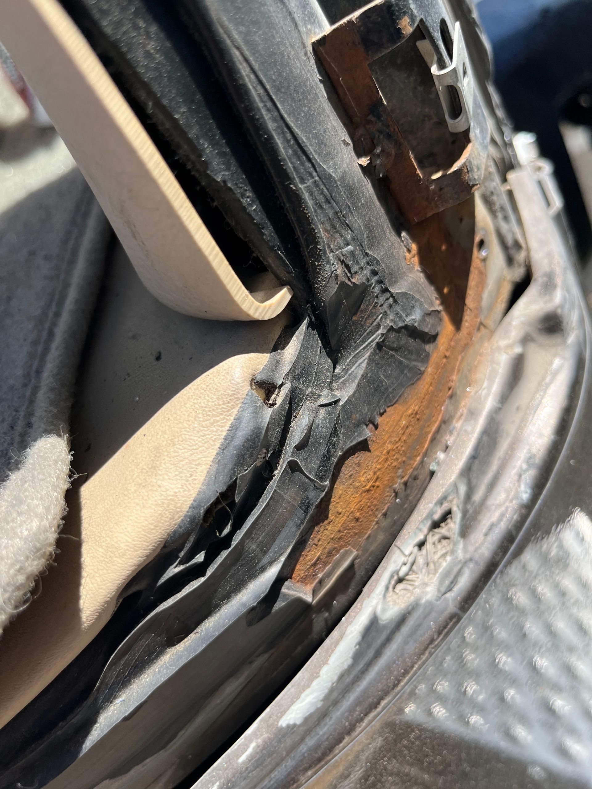 Close-up of a damaged black car door seal with rust and peeling trim on a metal step plate.