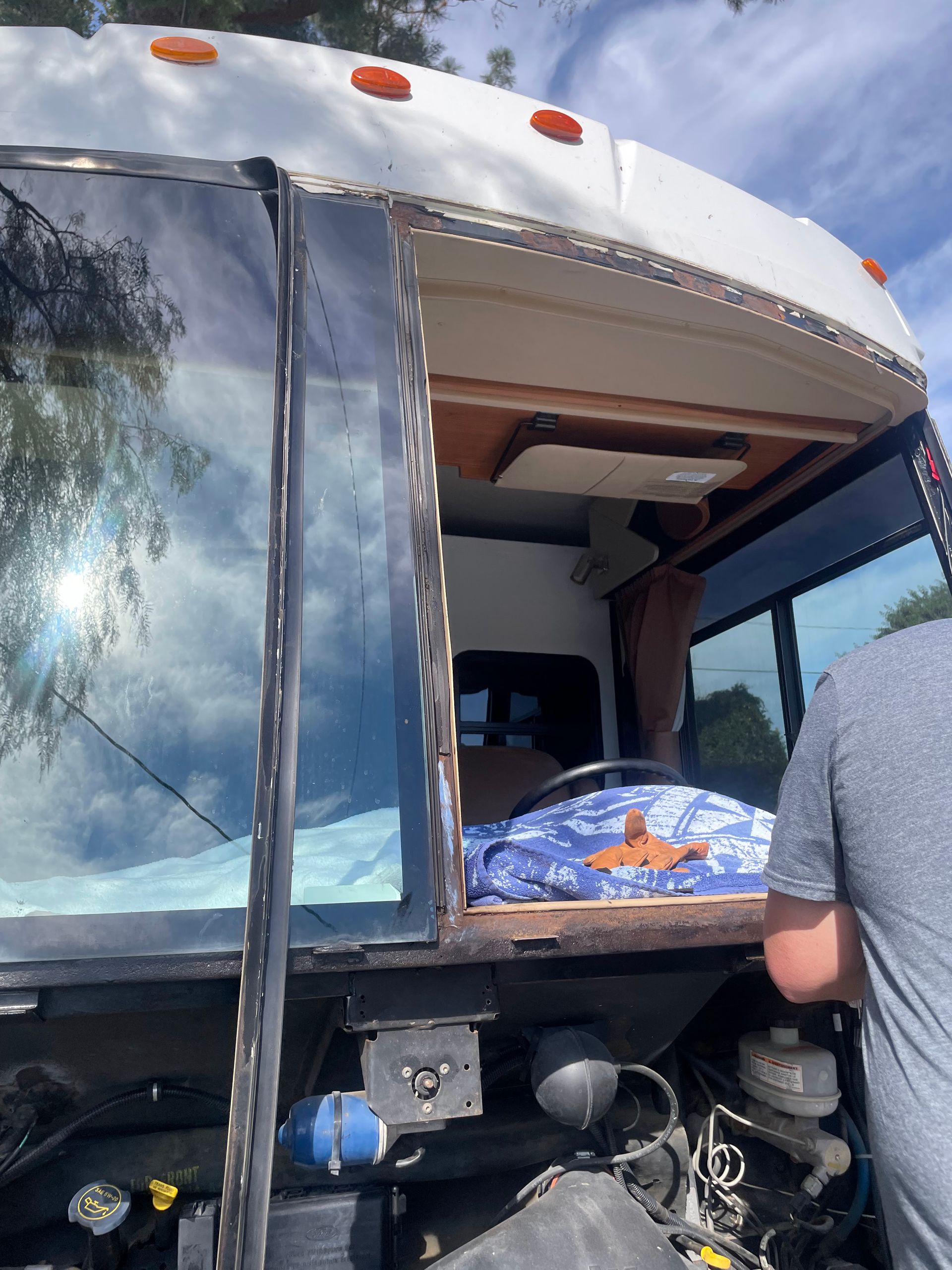 Person loading items into a bus storage compartment beside a blue bedspread and open window