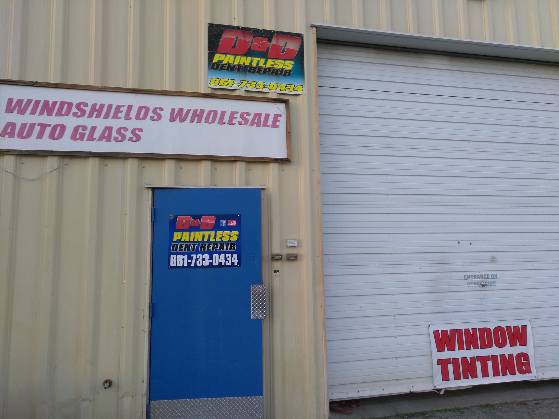 Windshields Wholesale Auto Glass storefront with blue door, white garage door, and window tinting sign
