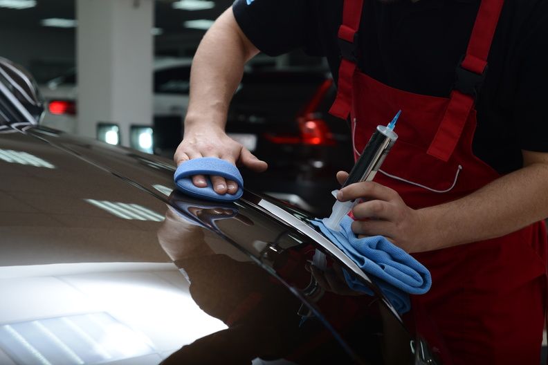 Person polishing a car hood with a cloth and spray bottle in a garage