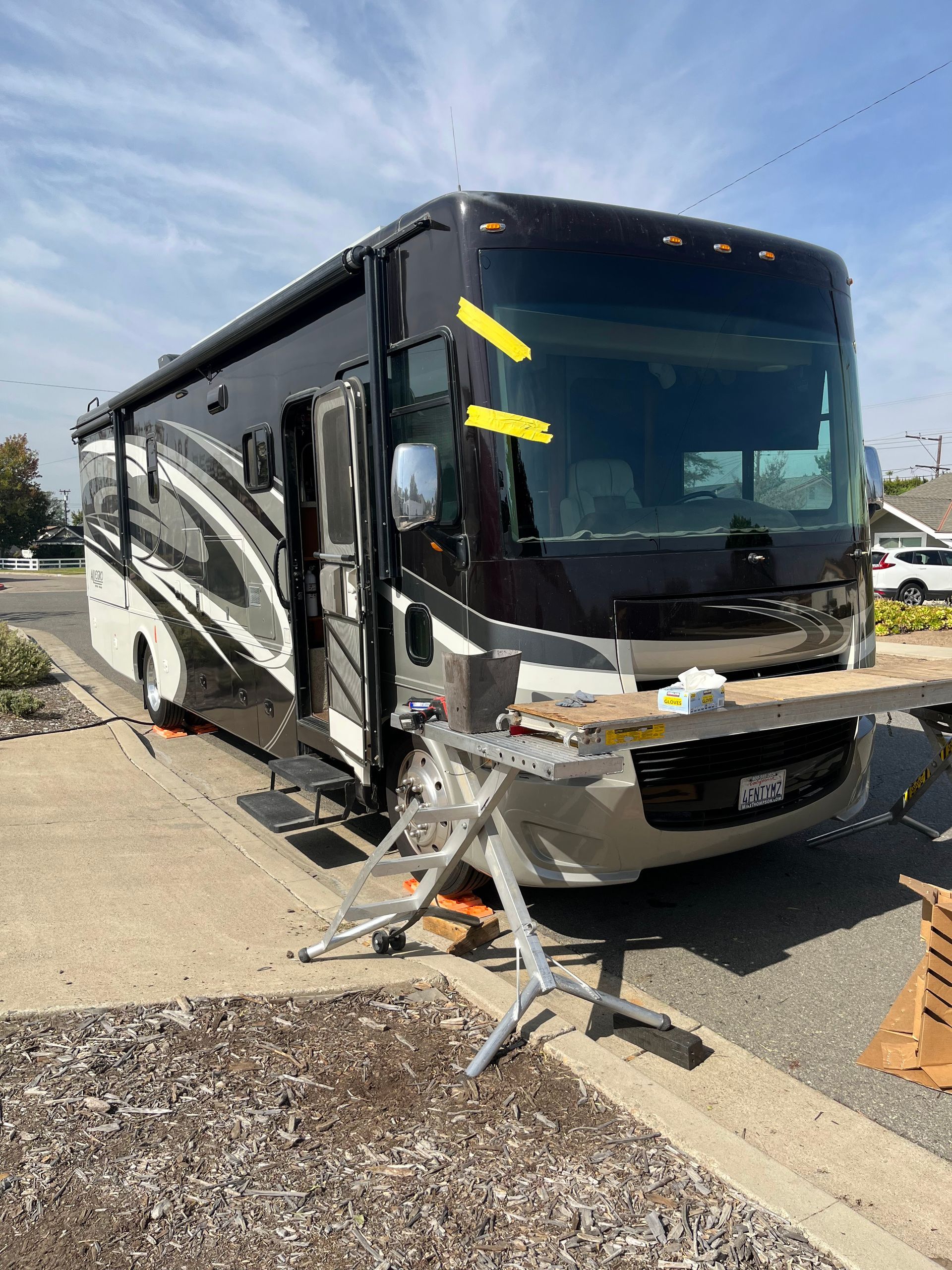 Damaged black and silver RV crashed into a curb, with front-end damage and debris on the roadside.