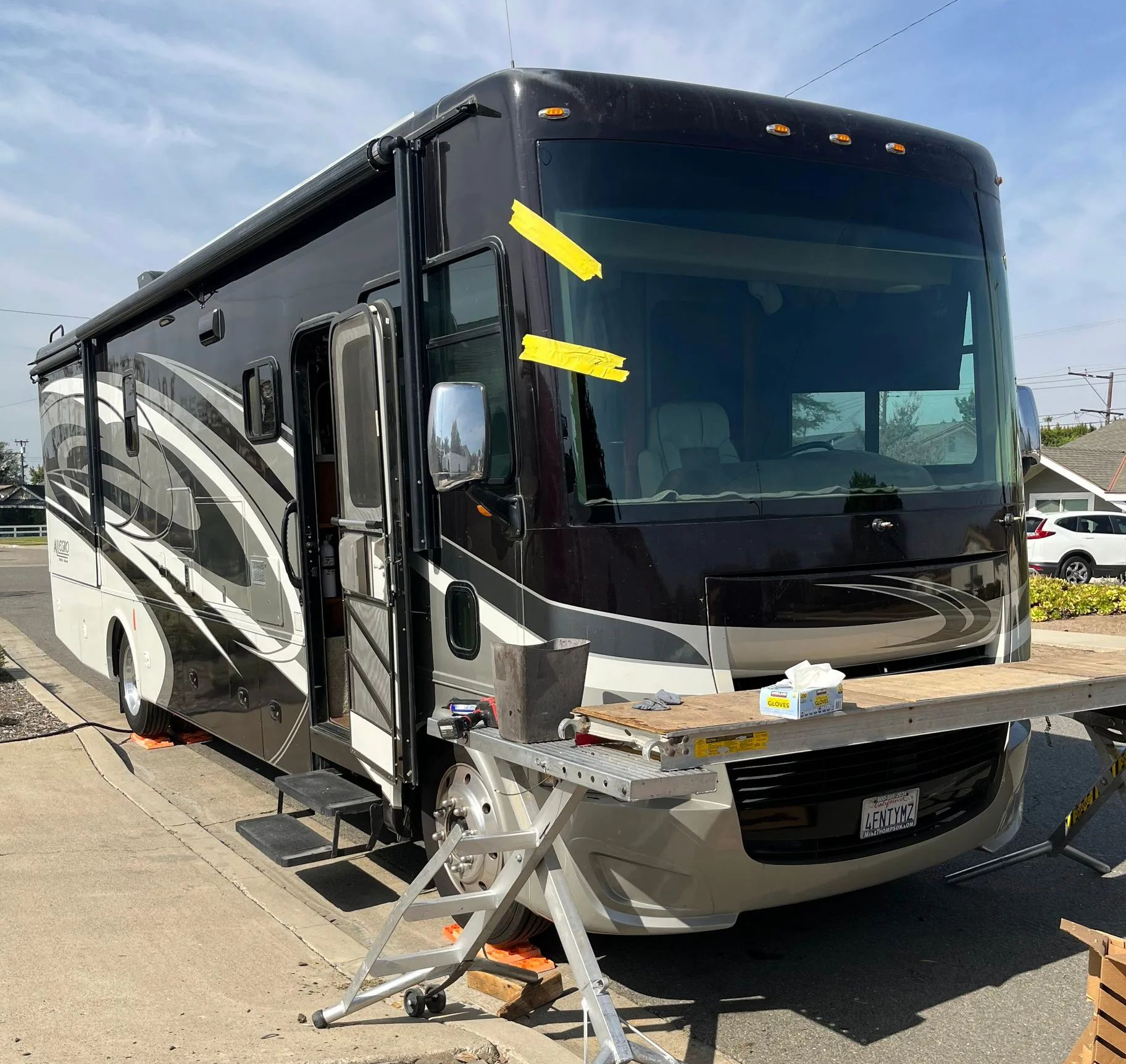Damaged black-and-white RV with front-end damage parked outdoors under bright sunlight
