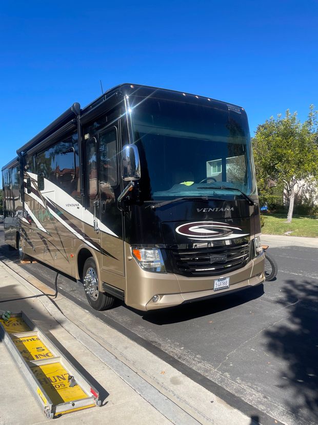 Black-and-tan tour bus parked at a curb on a sunny street