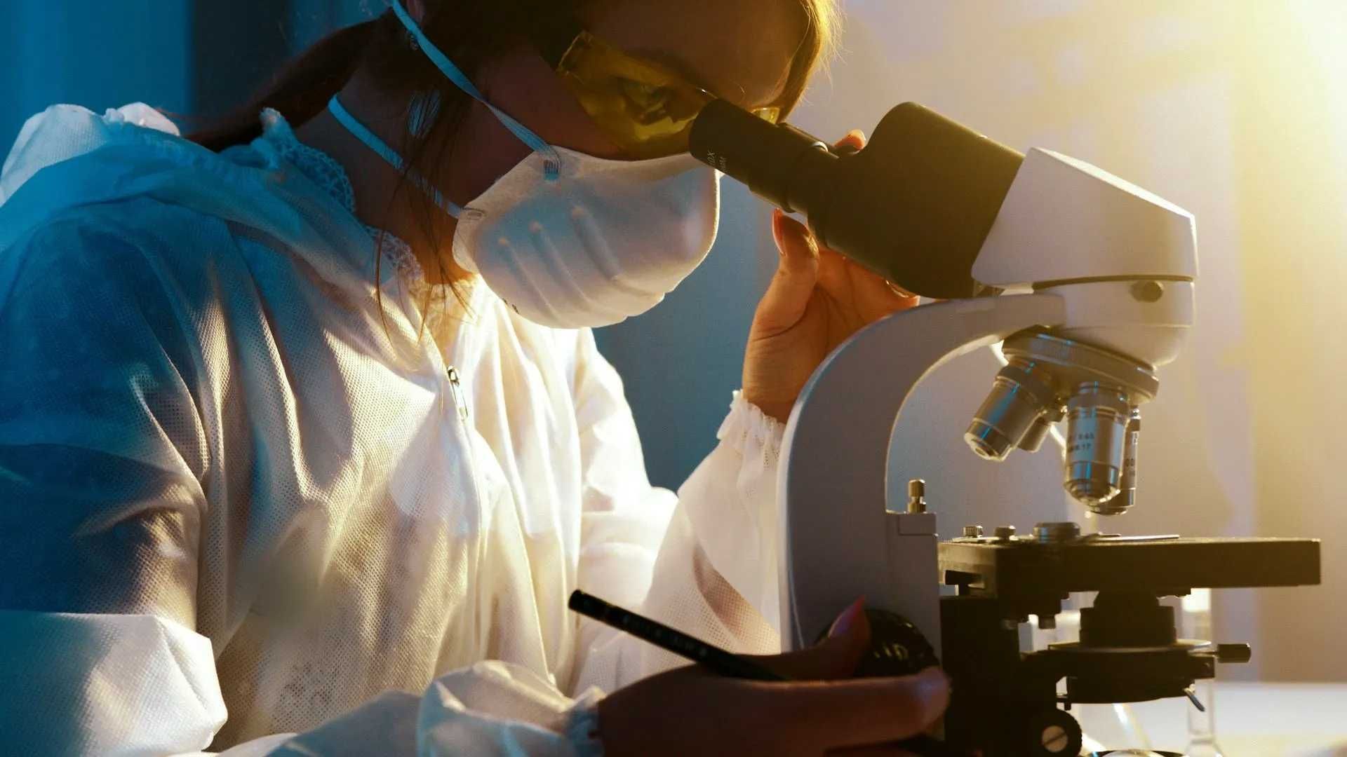 woman with mask and glasses looking through microscope
