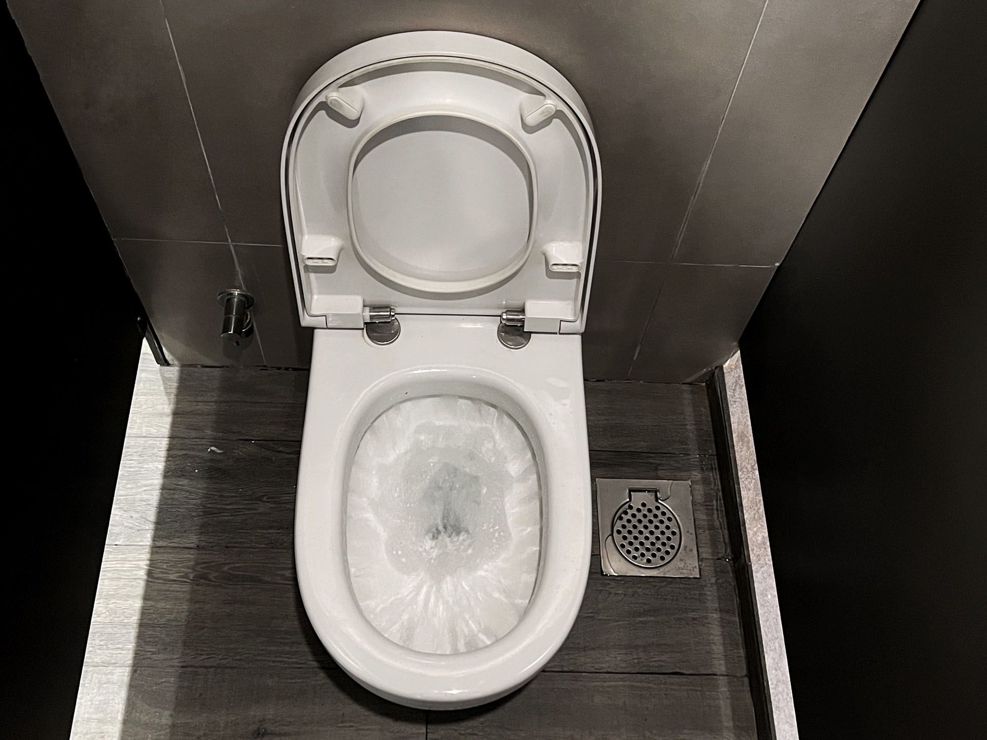 A toilet in a public restroom with the lid up