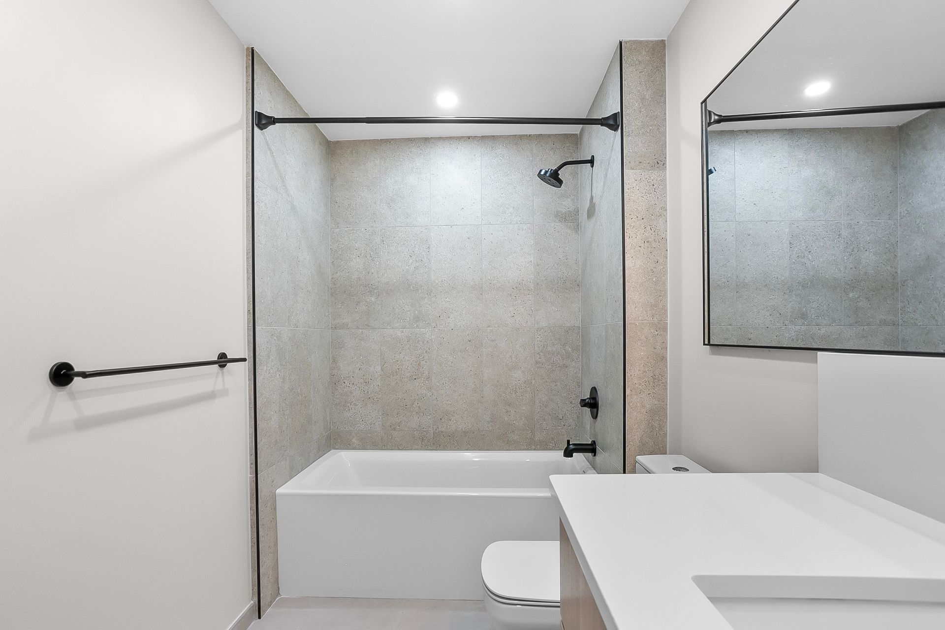Modern bathroom with a bathtub, showerhead, vanity, and large mirror. Gray and white color scheme.