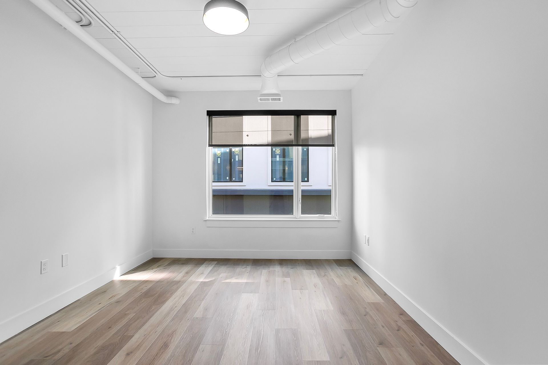 Empty, bright room with a large window and wood-look flooring. White walls and ceiling.