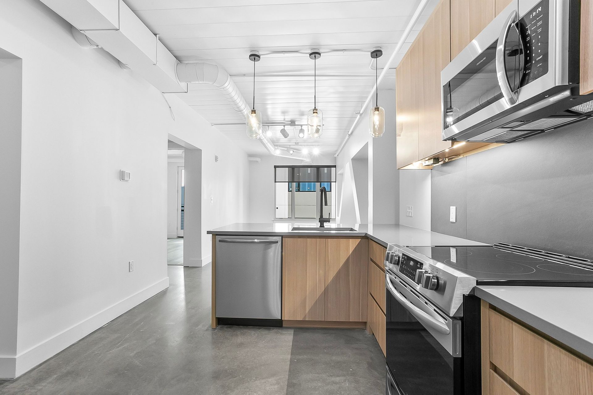 Modern kitchen with light wood cabinets, stainless steel appliances, and a gray concrete floor.