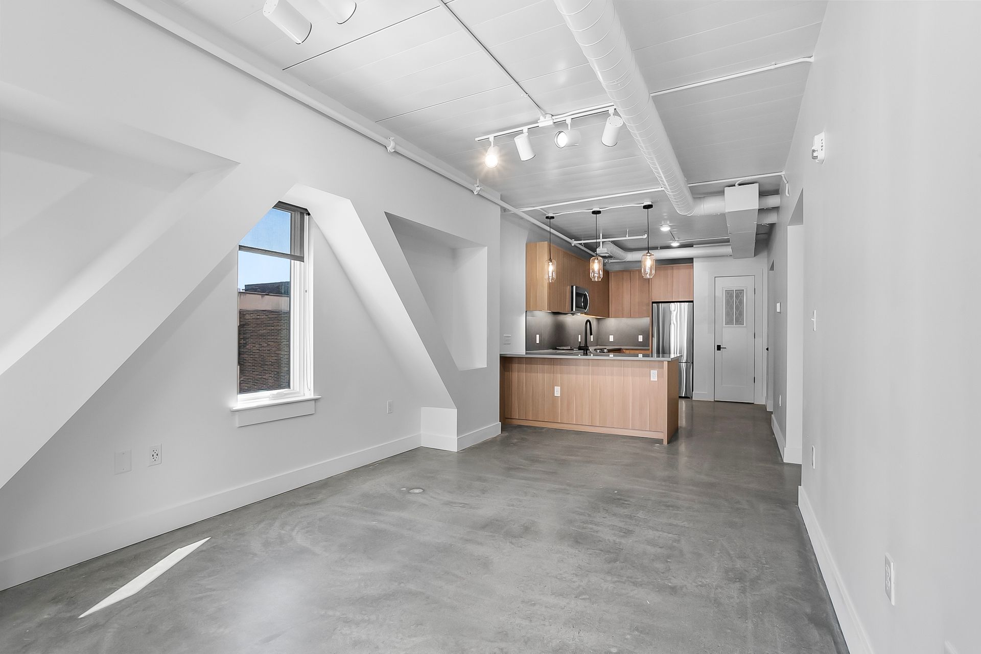 Empty modern apartment with angled walls, concrete floors, and open kitchen.