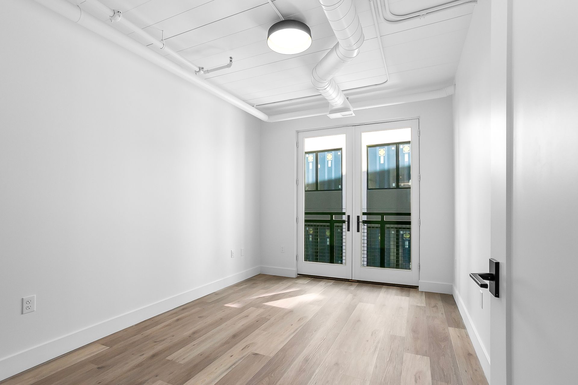 Empty room with light wood floors, white walls, and French doors to a balcony.