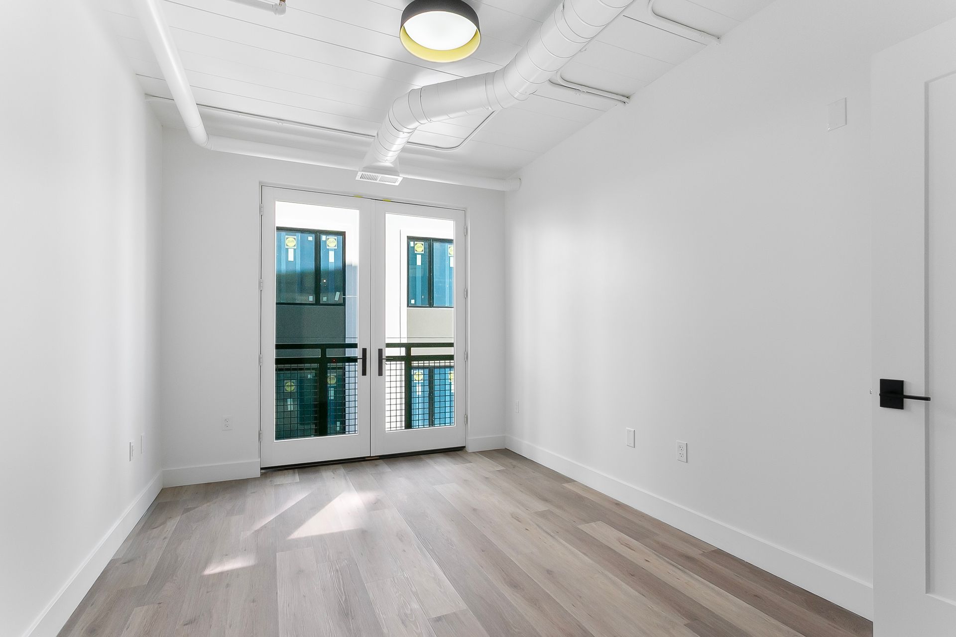 Empty room with white walls, light wood floor, and French doors leading to a balcony.