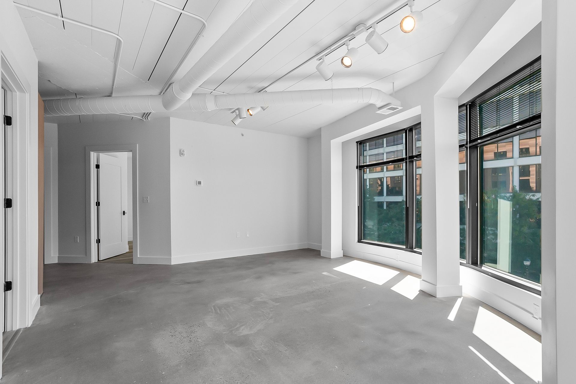 Empty, modern room with large windows, white walls, and gray floor.