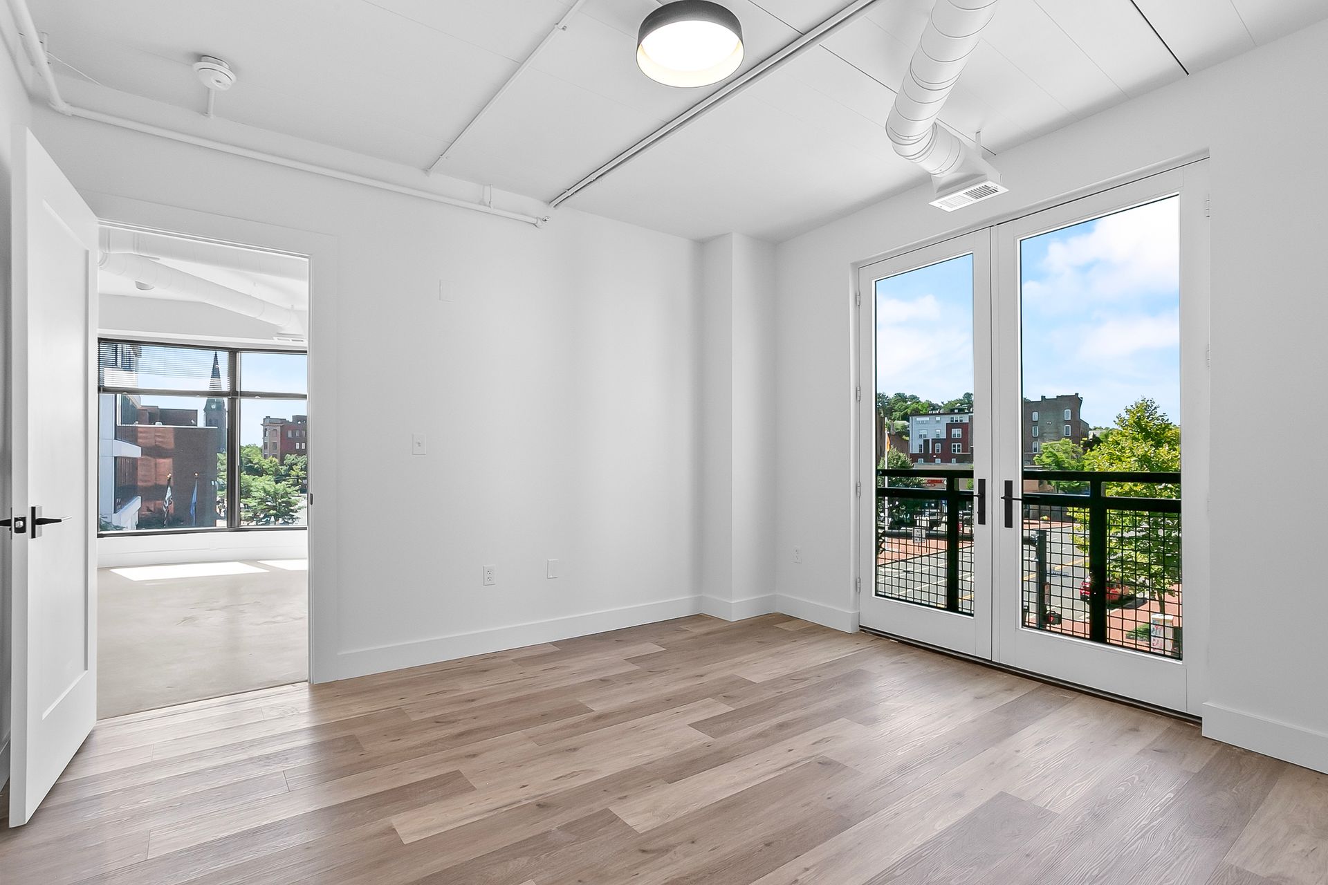 Empty room with light wood floors, white walls, and French doors leading to a balcony.