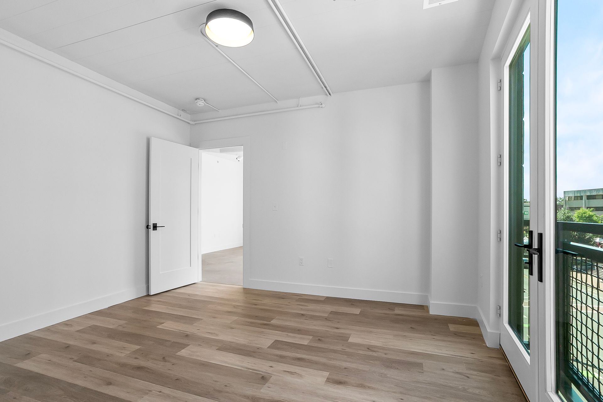 Empty room with light wood floors, white walls, and a door to a balcony.