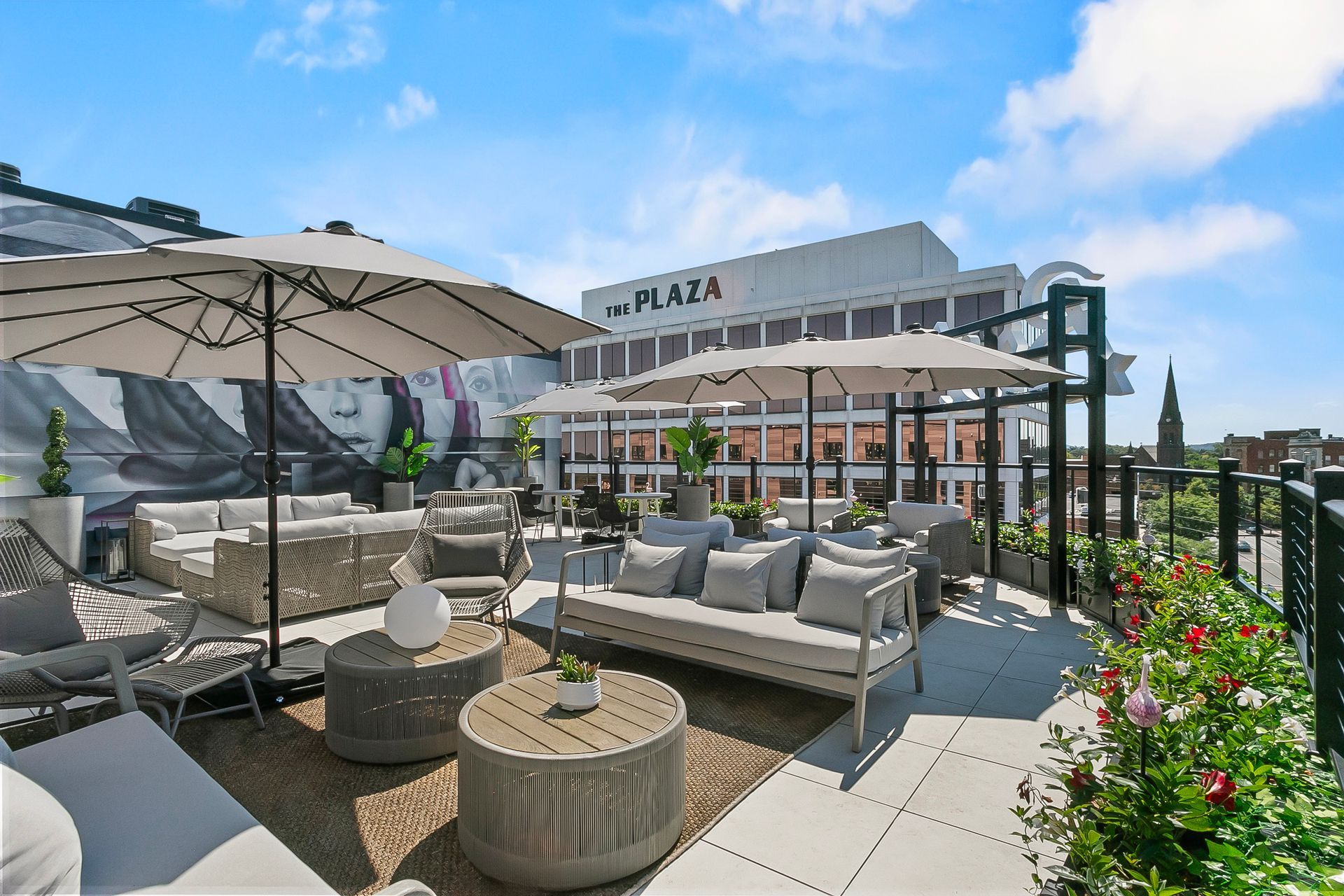 Rooftop patio with seating and umbrellas, The Plaza hotel in the background, sunny day.
