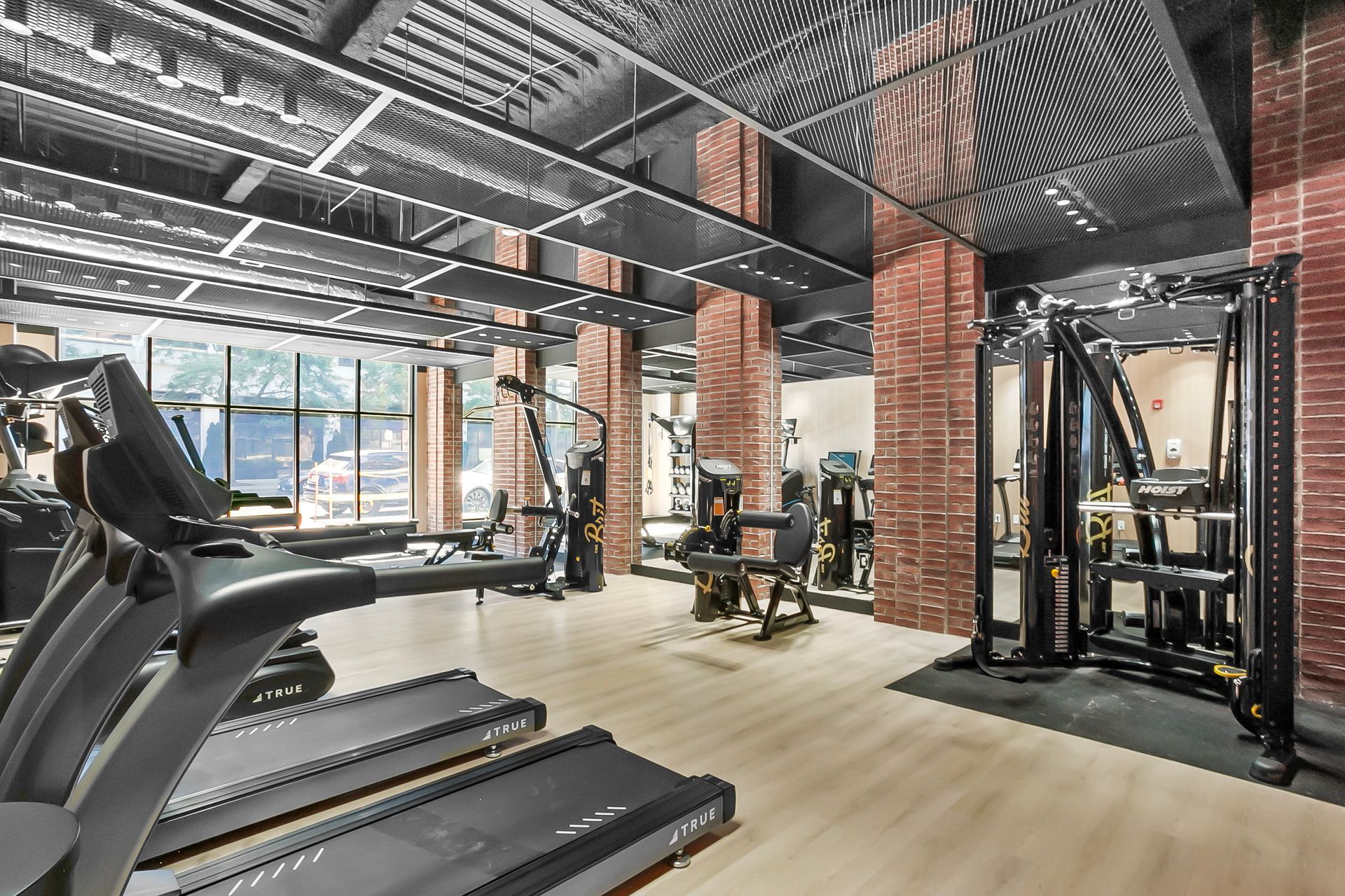 Gym interior with treadmills, weight machines, exposed brick columns, and mirrored ceiling.