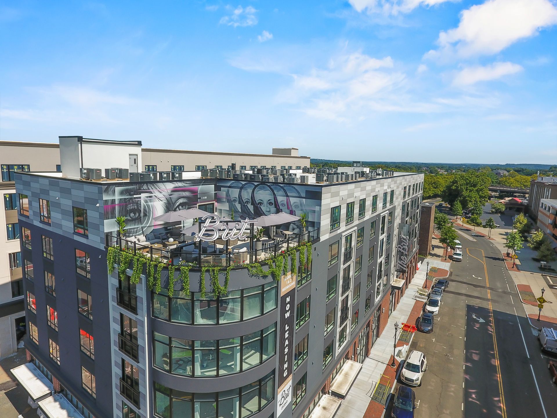 Multi-story modern building with rooftop seating, street view, and blue sky.