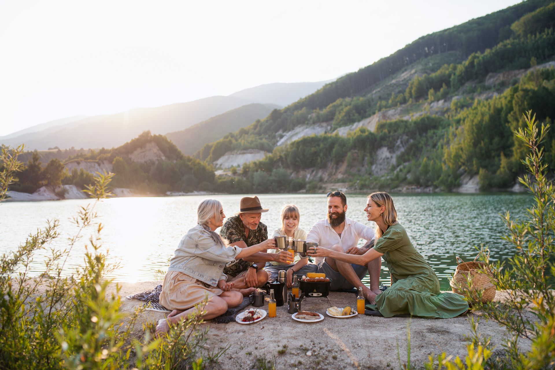 People sharing a picnic by a lake, with mountains and sunset light in the background