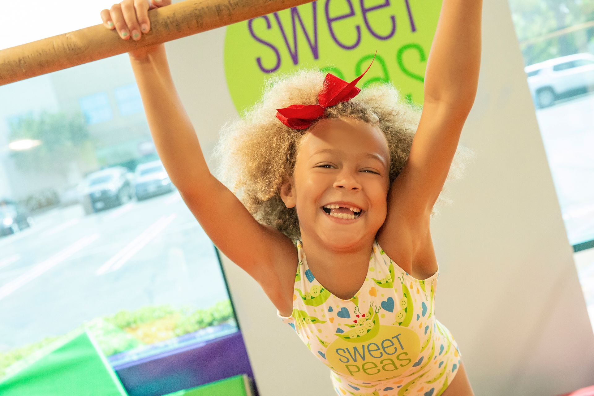Blonde child smiles, crawling on a green surface toward the viewer in a pit filled with foam cubes.