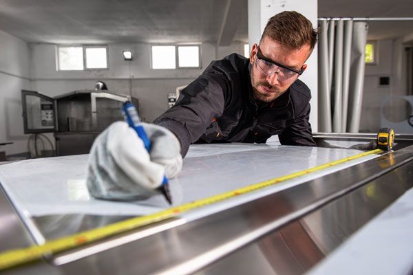 A Man Is Measuring A Piece Of Metal With A Tape Measure — ADR Engineering in Collinsville, QLD