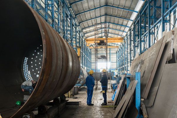 Two Men Are Standing In A Factory Next To A Large Metal Pipe — ADR Engineering in Collinsville, QLD