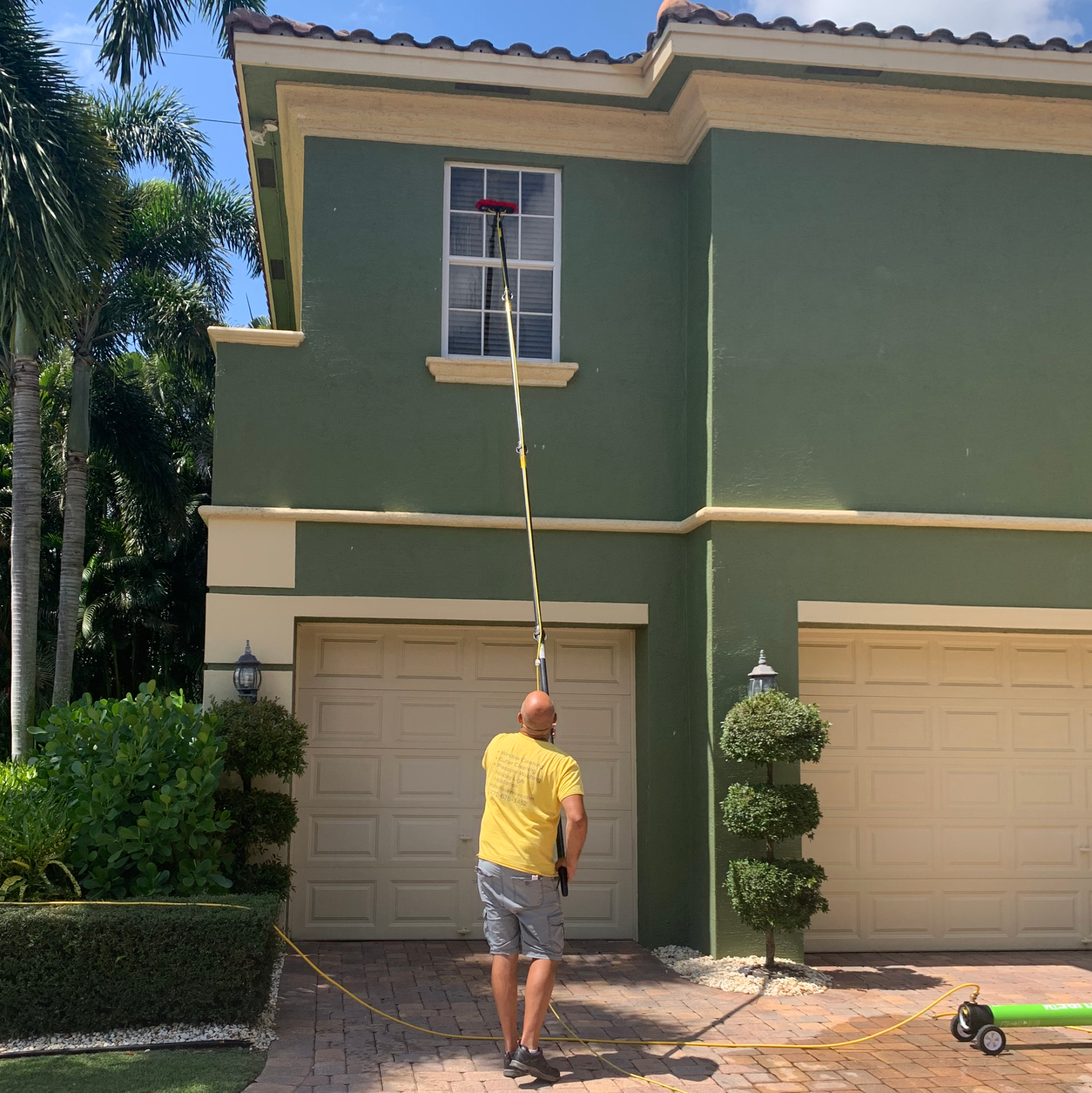 Man cleaning the windows with an extender on a green townhome with tan garage doors