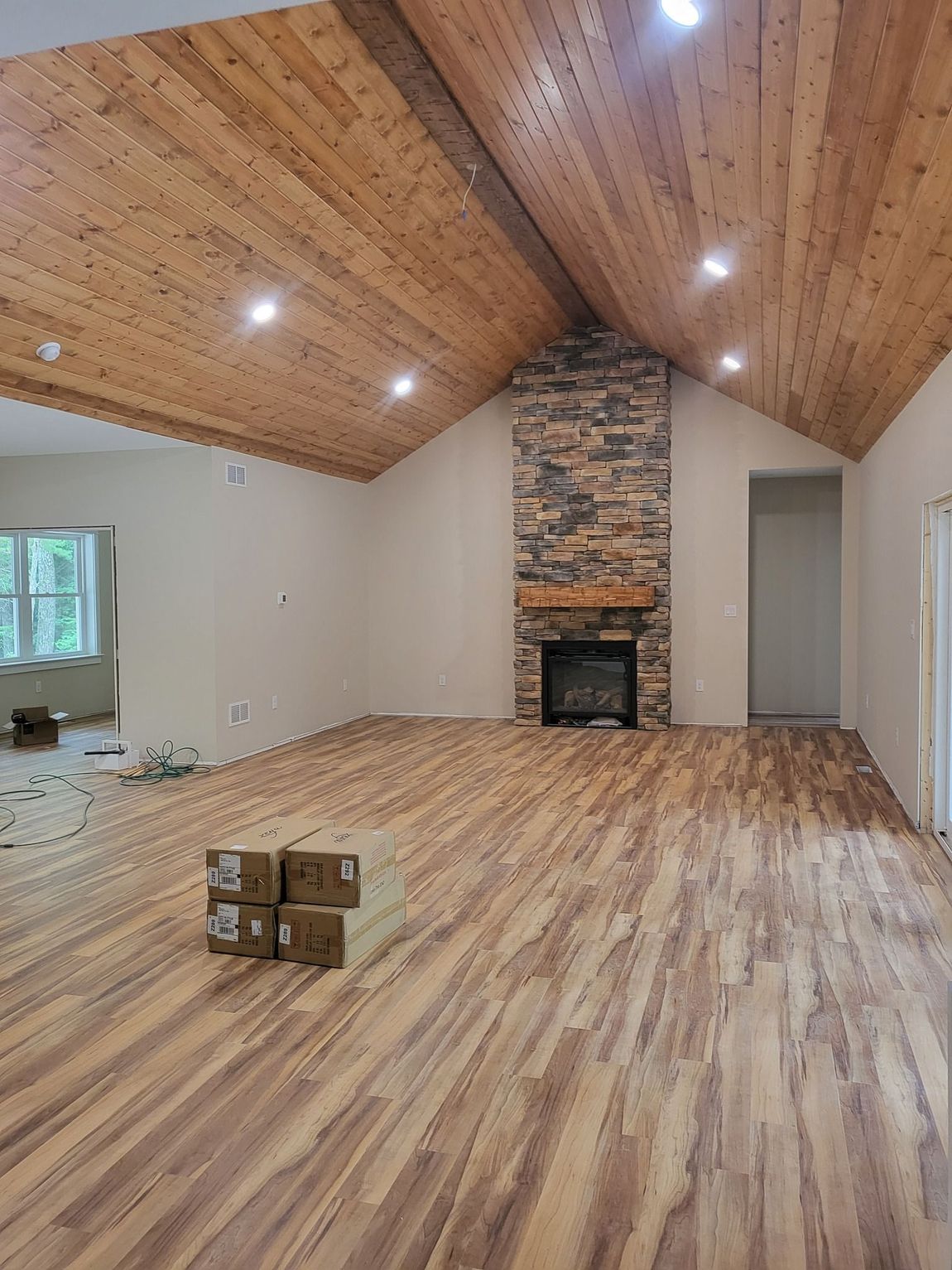 Empty living room with vaulted wood ceiling, stone fireplace, and wood-pattern flooring.