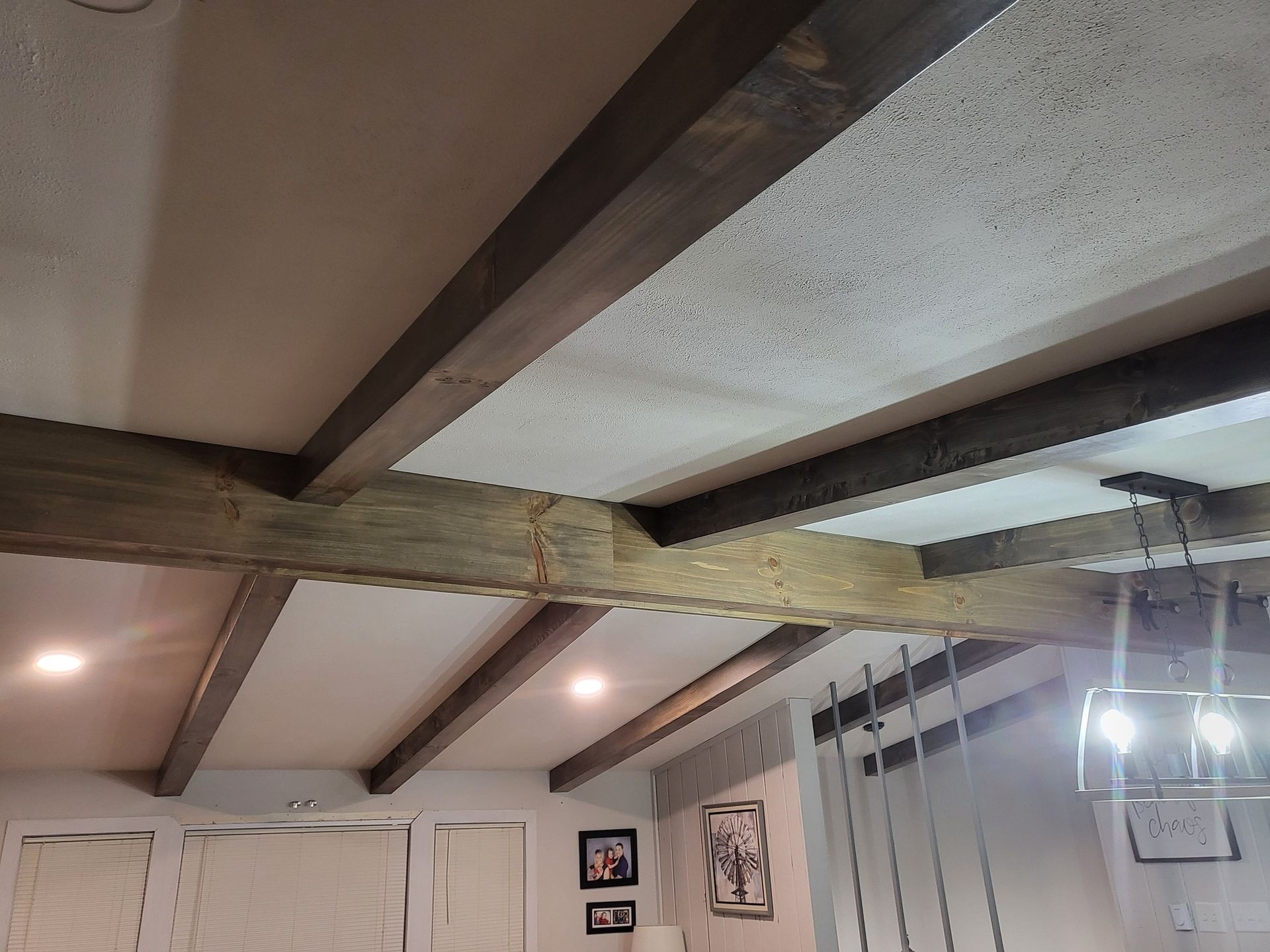 Ceiling with exposed wooden beams, recessed lights, and hanging pendant lamps in a bright interior room