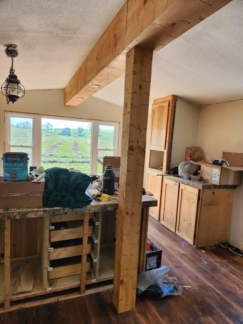 Open-plan kitchen with exposed wood beam, island, cabinets, and large window overlooking greenery