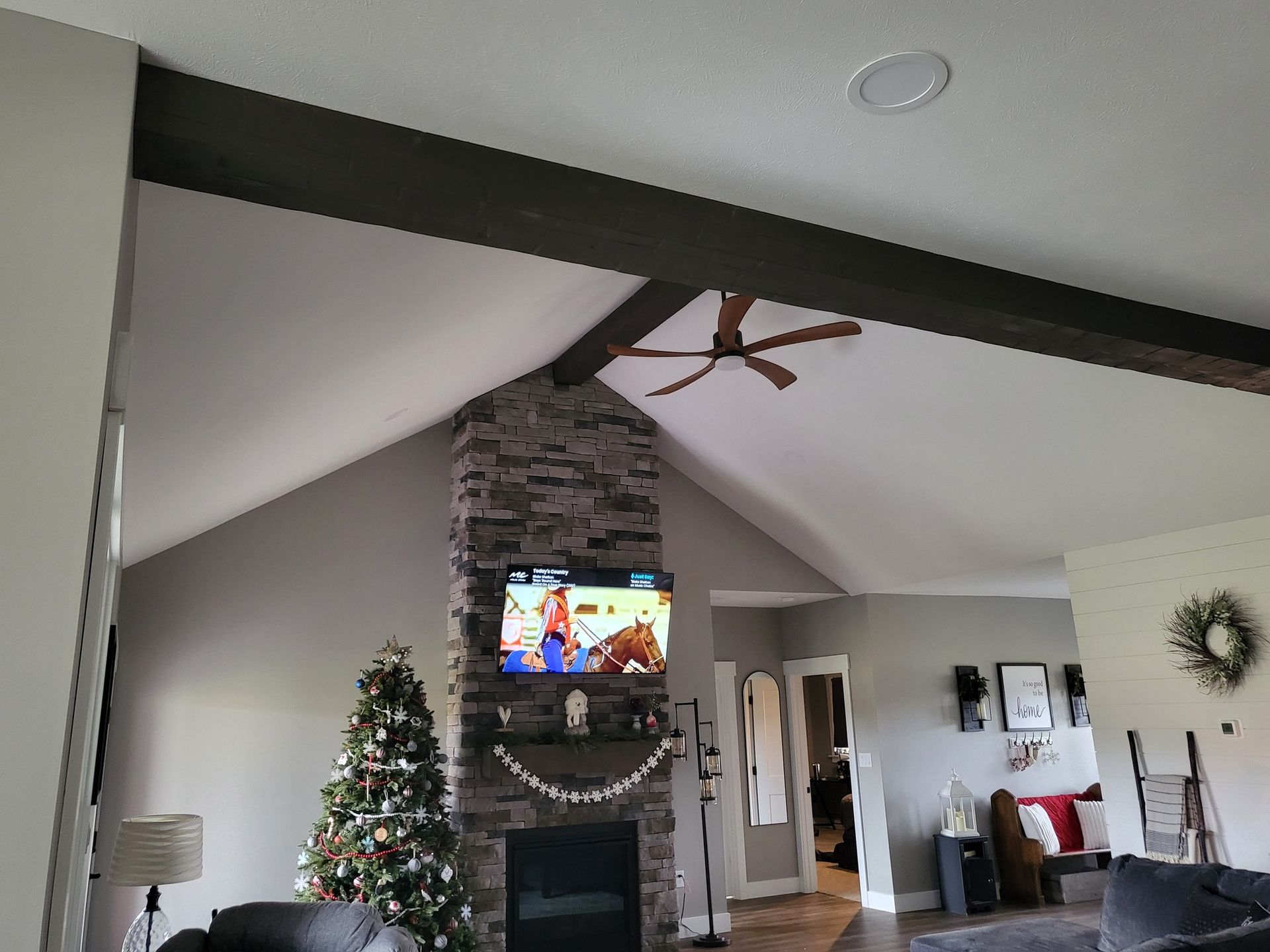 Living room with stone fireplace, TV, Christmas tree, and vaulted ceiling with fan